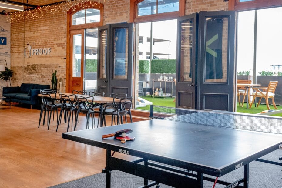 Espace de détente en bureau ouvert avec table de ping-pong, coin salon et terrasse extérieure avec mobilier de jardin.
