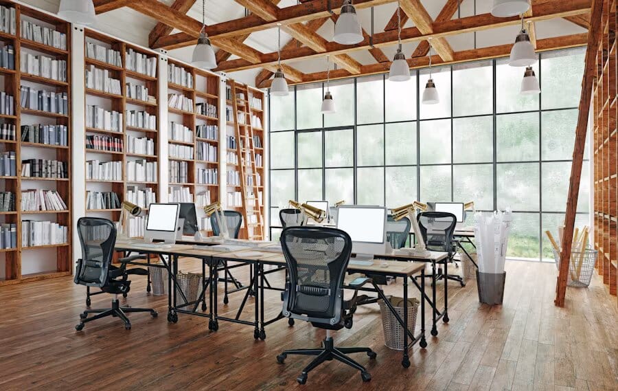 Bureau partagé avec grandes étagères remplies de livres, poutres en bois apparentes et grandes fenêtres industrielles